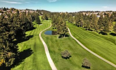 Aerial view of a golf course with winding cart paths, a small pond, and green fairways lined by trees.