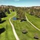 Aerial view of a golf course with winding cart paths, a small pond, and green fairways lined by trees.
