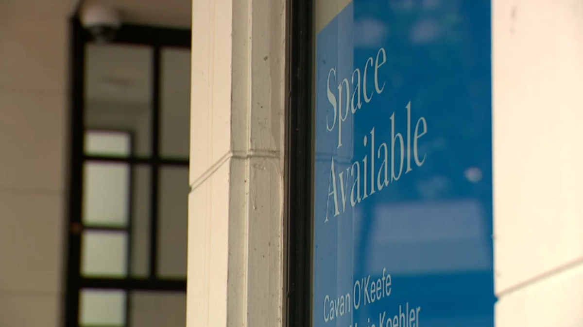 Blue storefront window sign reading 'Space Available' in white cursive text, with names at the bottom of the panel.