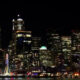 Night city skyline at night with illuminated skyscrapers along the waterfront and a lit ferris wheel by the water.
