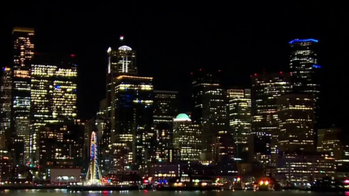 Night city skyline at night with illuminated skyscrapers along the waterfront and a lit ferris wheel by the water.