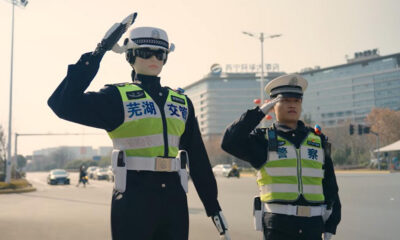 Two police officers in reflective vests saluting while standing in the street, directing traffic.
