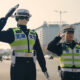 Two police officers in reflective vests saluting while standing in the street, directing traffic.