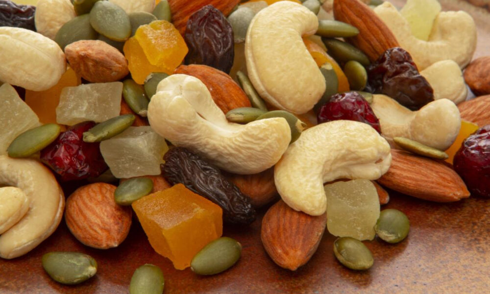 Trail mix with cashews, almonds, pumpkin seeds and assorted dried fruits on a brown surface.