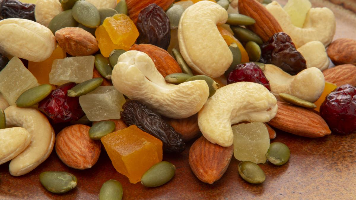 Trail mix with cashews, almonds, pumpkin seeds and assorted dried fruits on a brown surface.