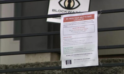 Flyer taped to a metal railing with a red headline asking for help to save 14th Ave W, featuring a logo above and a QR code at the bottom.