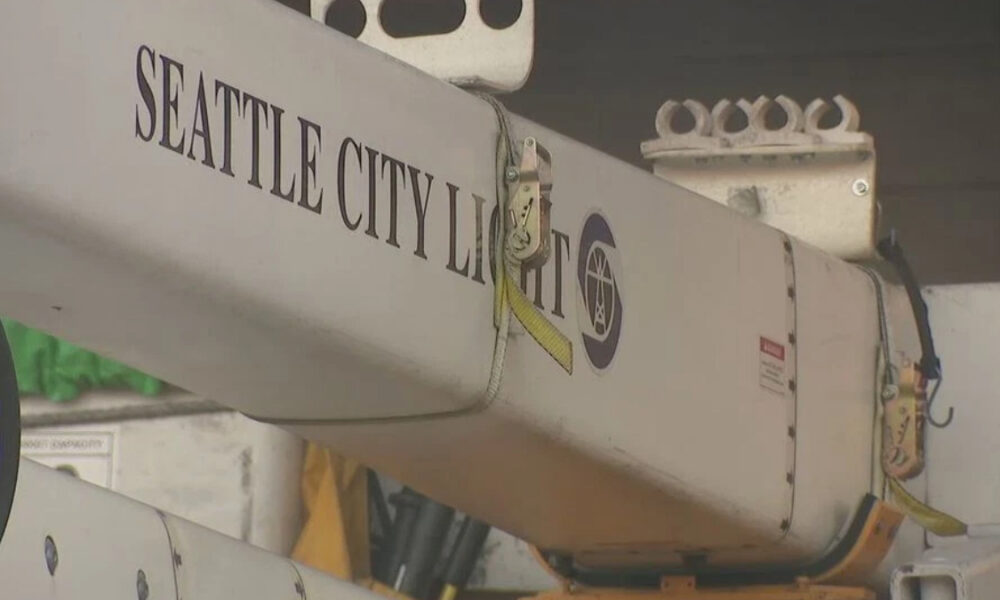 Close-up of a utility crane arm labeled Seattle City Light with a yellow safety strap and metal hooks visible on the side.
