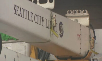 Close-up of a utility crane arm labeled Seattle City Light with a yellow safety strap and metal hooks visible on the side.
