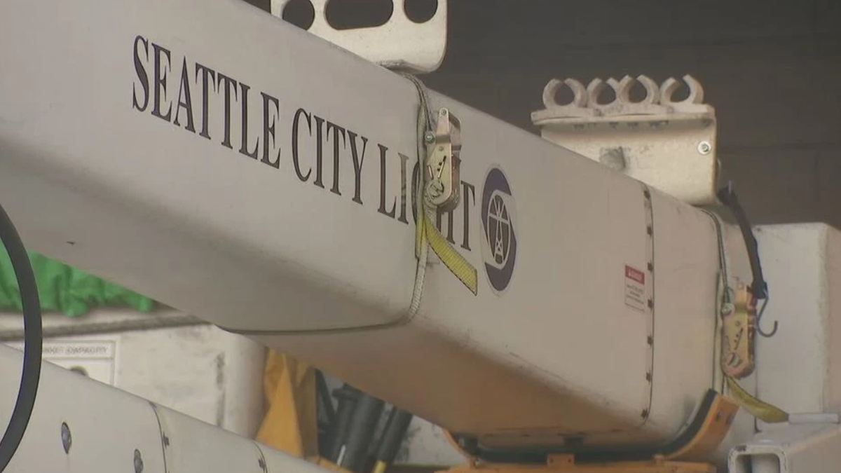 Close-up of a utility crane arm labeled Seattle City Light with a yellow safety strap and metal hooks visible on the side.