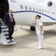Man in a dark suit steps from a Royal Air Force jet via mobile stairs while a uniformed officer salutes and another suited man watches on the tarmac