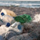 Pile of plastic bottles, cups, and tangled fishing nets littering a sandy beach with the sea in the background.