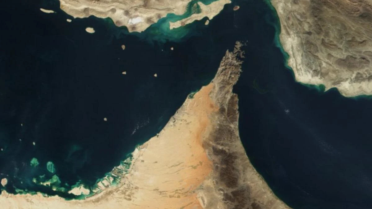 Satellite view of a sandy peninsula jutting into dark sea, with arid desert surrounding and turquoise coastal waters nearby