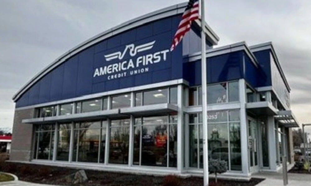 Exterior of the America First Credit Union branch with a blue curved roof and large glass windows, flagpole with an American flag outside.