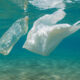 Plastic bottle and plastic bag float underwater in clear blue water, highlighting ocean plastic pollution.