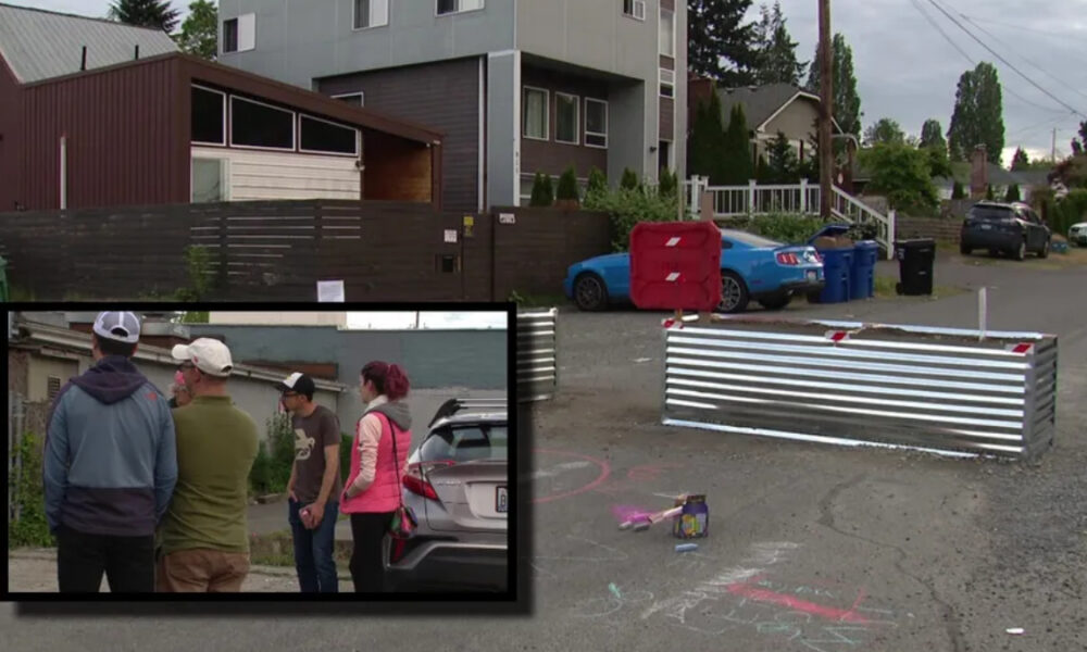 Street scene with a metal barricade blocking the road, chalk drawings on the pavement, a blue car, and several trash bins nearby.