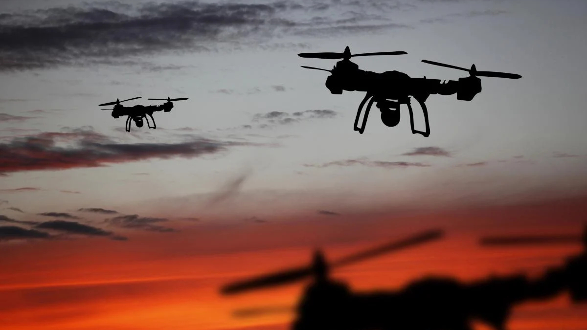 Two quadcopter drones silhouetted against a sunset orange sky, in flight.