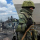 Soldier in camouflage gear with a rifle beside a gray train car as a destroyed village burns on the left (split image).