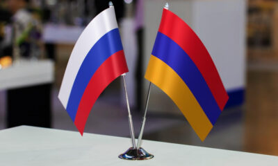 Two small national flags (Russia and Armenia) on a silver stand on a table.