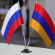 Two small national flags (Russia and Armenia) on a silver stand on a table.