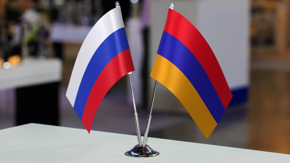Two small national flags (Russia and Armenia) on a silver stand on a table.