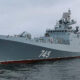 Grey naval warship with hull number 745 on calm sea under a cloudy sky, bow to the left.
