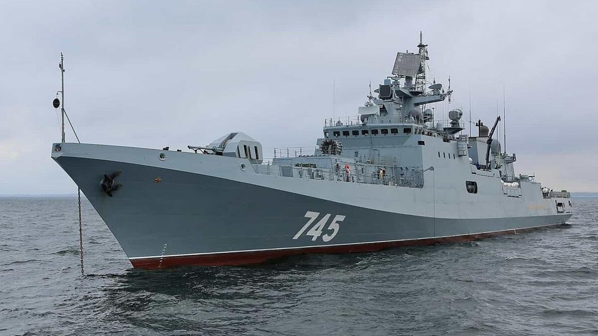 Grey naval warship with hull number 745 on calm sea under a cloudy sky, bow to the left.