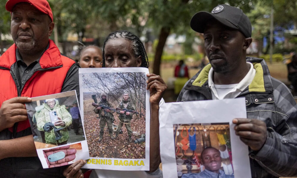 Three adults outdoors hold printed posters showing people’s photos during a daytime vigil or gathering in a park.