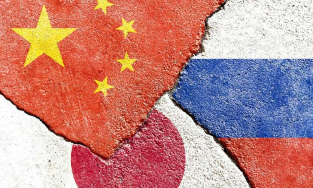 Cracked concrete wall with overlapping flags: China (red with yellow stars) on the left, Japan (red circle on white) at the bottom, and Russia (white-blue-red stripes) on the right, all weathered.