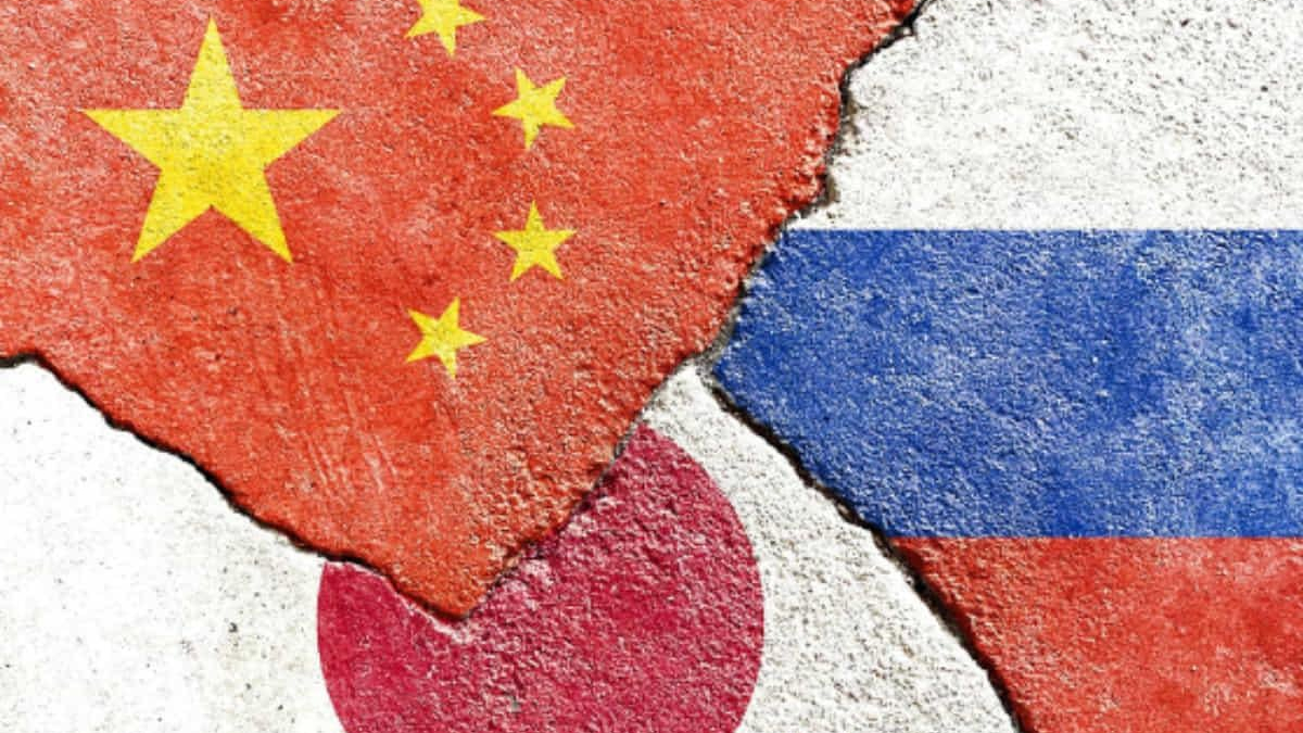 Cracked concrete wall with overlapping flags: China (red with yellow stars) on the left, Japan (red circle on white) at the bottom, and Russia (white-blue-red stripes) on the right, all weathered.