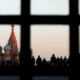 Silhouetted crowd on Red Square at dusk, with Saint Basil's Cathedral and the Spasskaya Tower visible through a window grid.