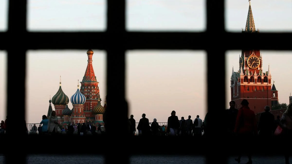Silhouetted crowd on Red Square at dusk, with Saint Basil's Cathedral and the Spasskaya Tower visible through a window grid.