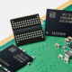 Close-up of memory chips on a green circuit board with a gold edge connector, showing electronic components and circuitry nearby.