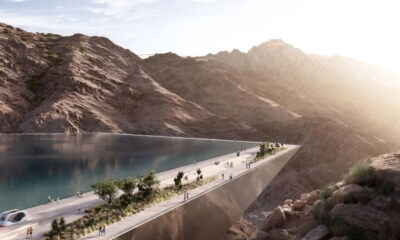 Futuristic elevated walkway over a deep canyon with a calm lake to the left; pedestrians stroll along the path as sunlight shines from the right.