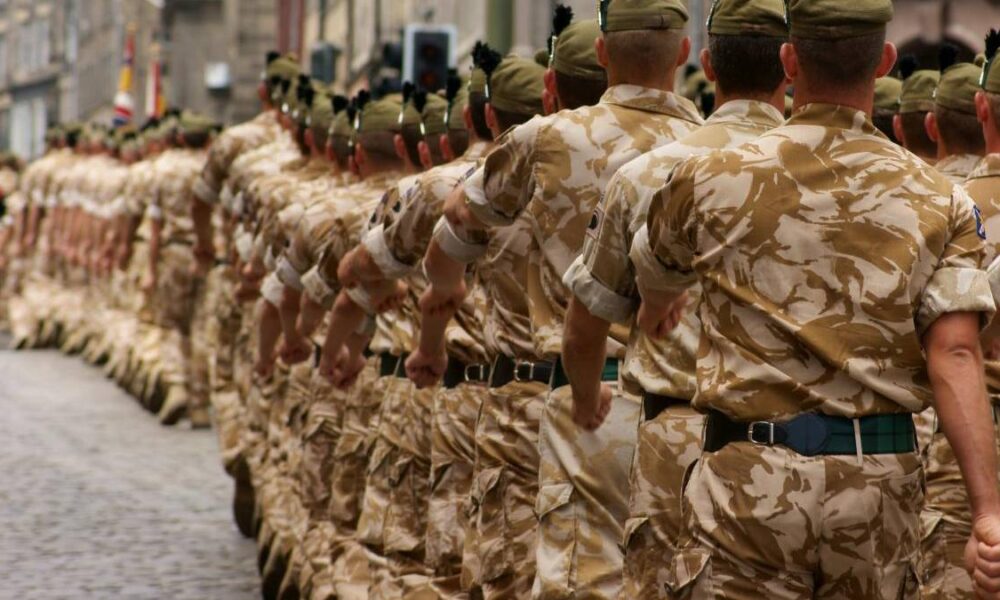 Line of soldiers in desert camouflage marching in a parade along a cobblestone street.