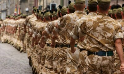 Line of soldiers in desert camouflage marching in a parade along a cobblestone street.