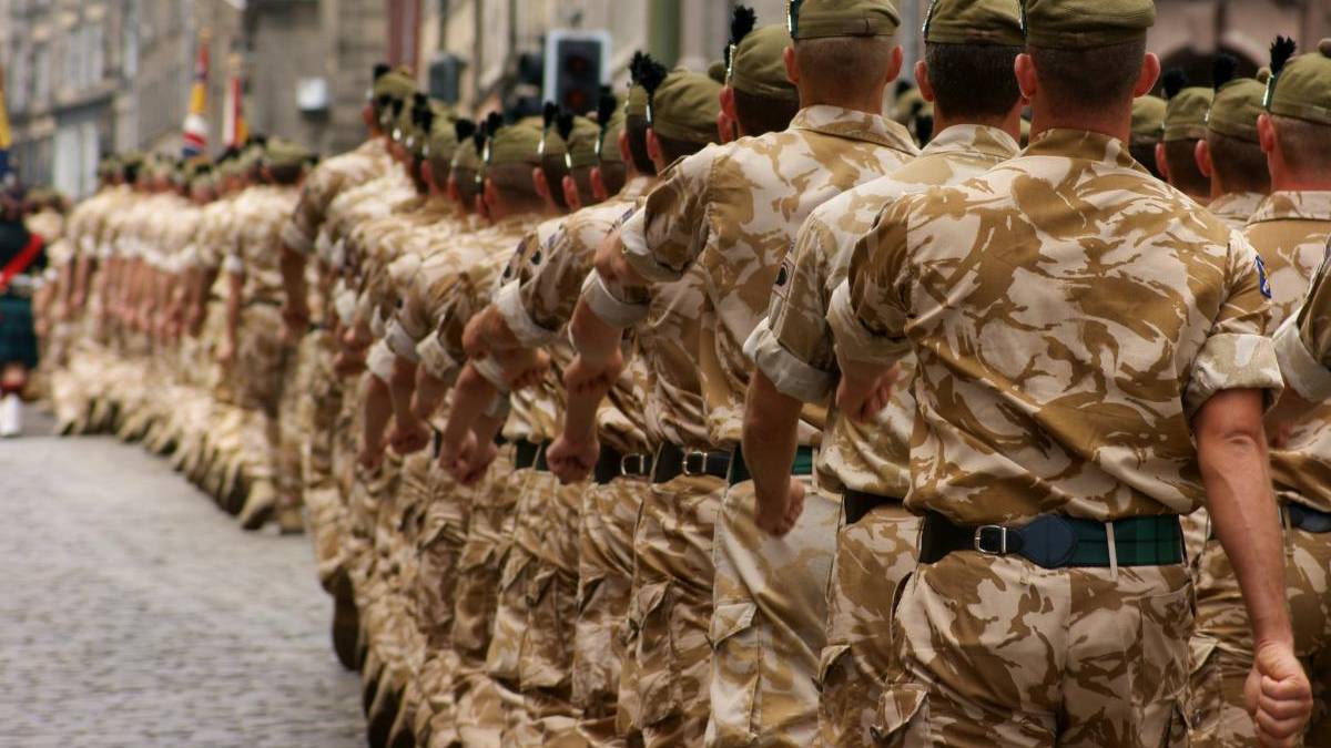 Line of soldiers in desert camouflage marching in a parade along a cobblestone street.