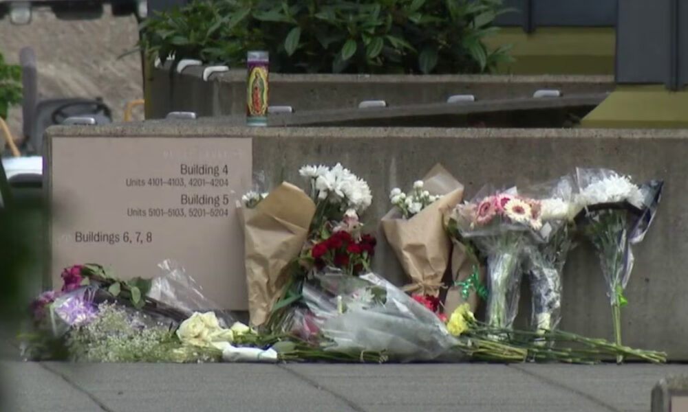 Flowers and bouquets placed along a concrete wall beside a sign listing building numbers 4, 5, and 6–8, creating a small memorial site.
