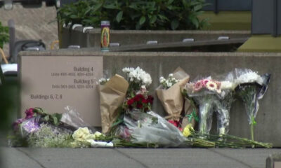 Flowers and bouquets placed along a concrete wall beside a sign listing building numbers 4, 5, and 6–8, creating a small memorial site.