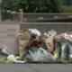 Flowers and bouquets placed along a concrete wall beside a sign listing building numbers 4, 5, and 6–8, creating a small memorial site.