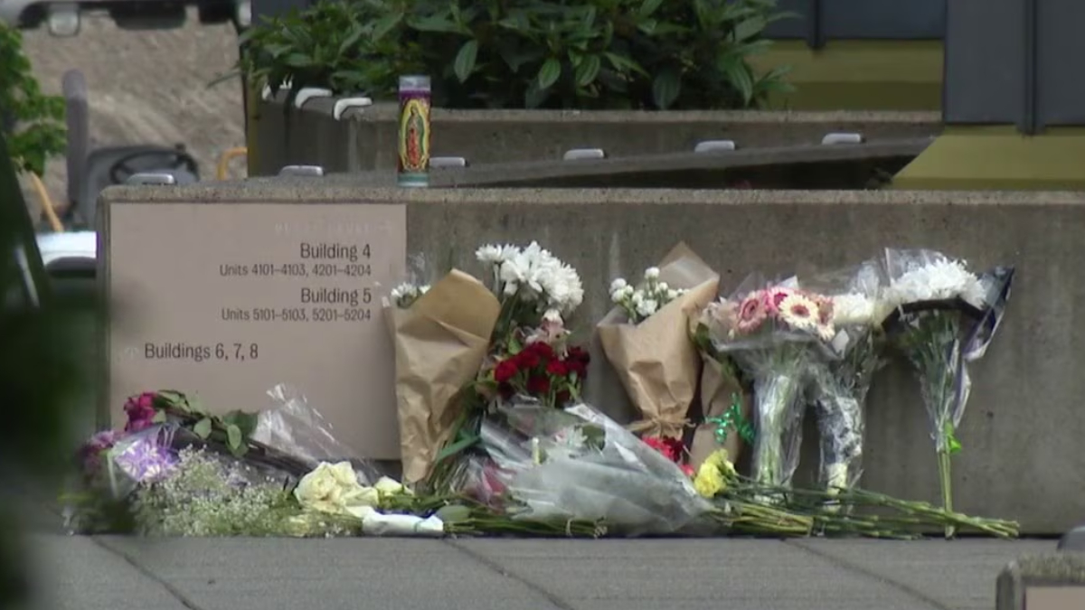Flowers and bouquets placed along a concrete wall beside a sign listing building numbers 4, 5, and 6–8, creating a small memorial site.