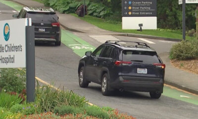 Dark SUV driving in a bike lane near Seattle Children's Hospital, with directional signs in the background.