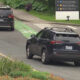 Dark SUV driving in a bike lane near Seattle Children's Hospital, with directional signs in the background.