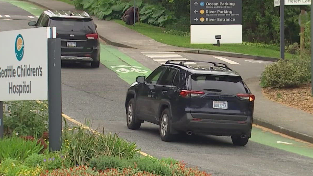 Dark SUV driving in a bike lane near Seattle Children's Hospital, with directional signs in the background.