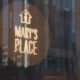 Circular brown sticker on a glass storefront reading 'MARY'S PLACE' with a small house icon above; city reflections visible in the glass.