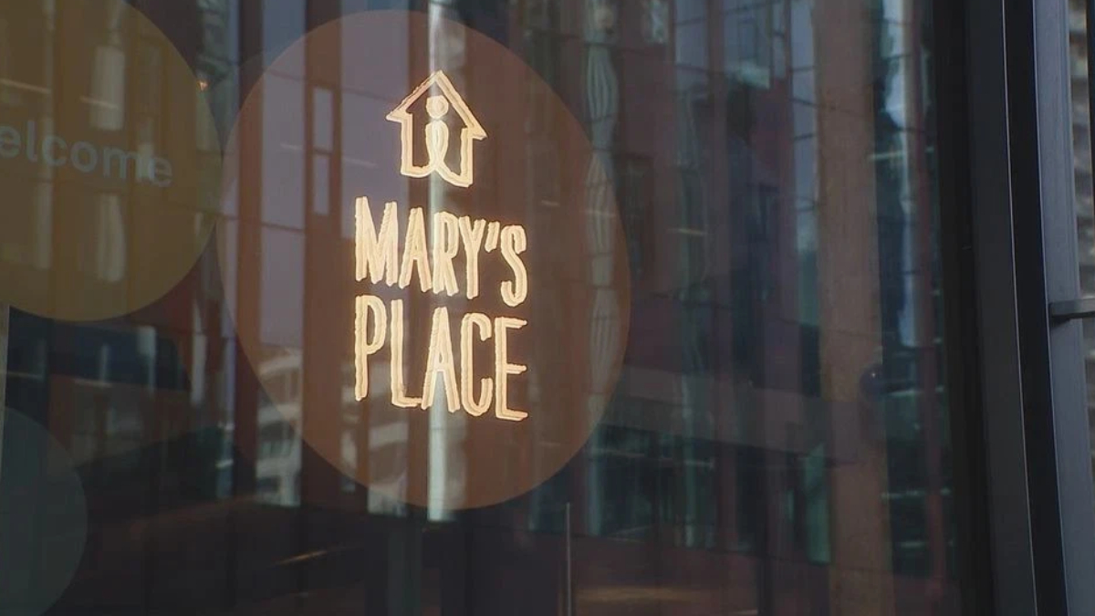 Circular brown sticker on a glass storefront reading 'MARY'S PLACE' with a small house icon above; city reflections visible in the glass.