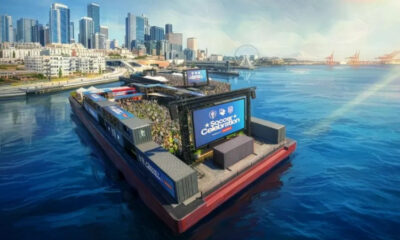 Floating water-stage with a large crowd watching a soccer celebration event by the city skyline and harbor.