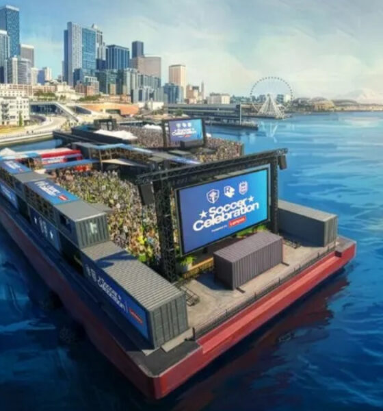 Floating water-stage with a large crowd watching a soccer celebration event by the city skyline and harbor.