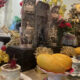 Altar setup with a golden laughing Buddha, incense, flowers, and large mango offerings on the table.