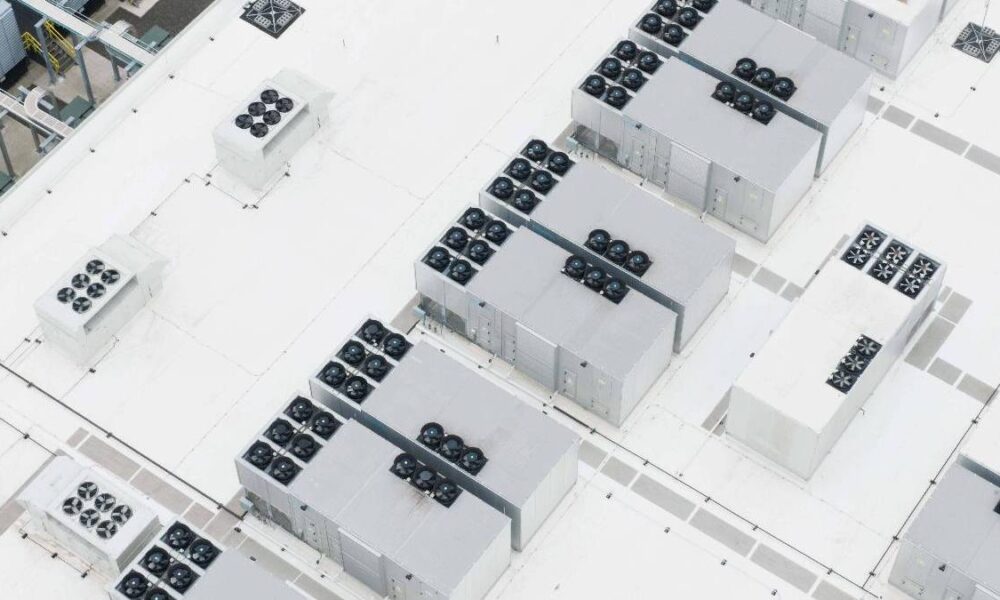 Aerial view of a white rooftop with multiple rectangular cooling units and rows of rooftop fans arranged across the surface.