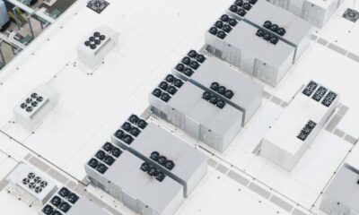 Aerial view of a white rooftop with multiple rectangular cooling units and rows of rooftop fans arranged across the surface.